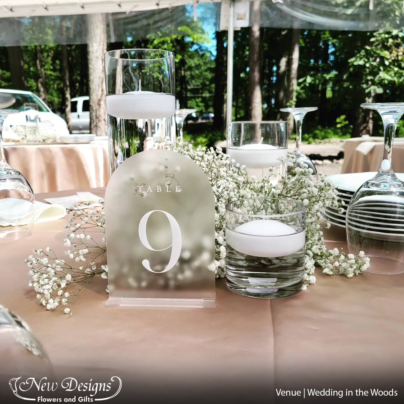 A gorgeous bundle of Babies breath cloud around 3 Pillar Vases of various heights, with floating candles, on a soft blush table cloth, at an outdoor venue in the woods.